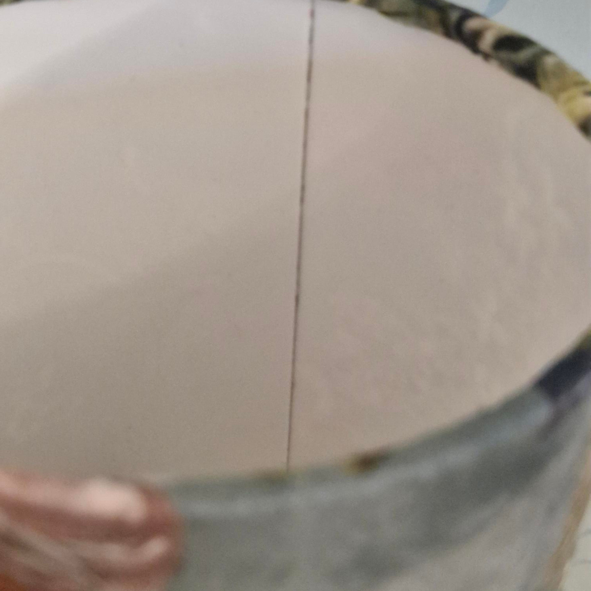 Close-up of the inside of a lampshade , showing a plain off-white interior surface with a narrow seam down the center and a patterned rim at the top edge.