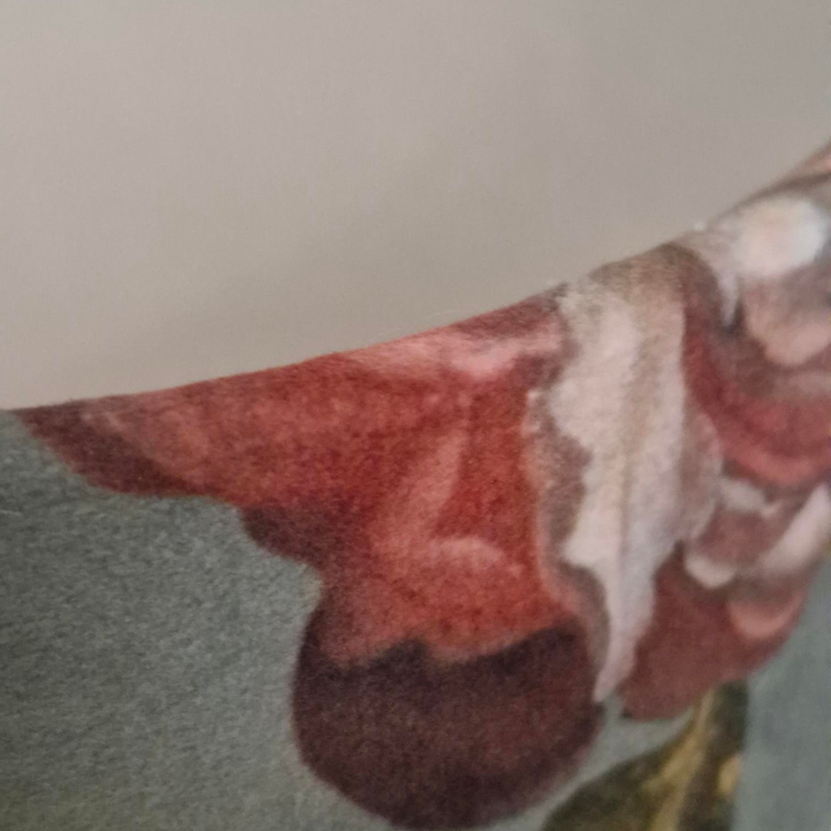 A close-up of a printed fabric or wallpaper pattern featuring a textured red and white abstract floral design on a muted gray-green background.
